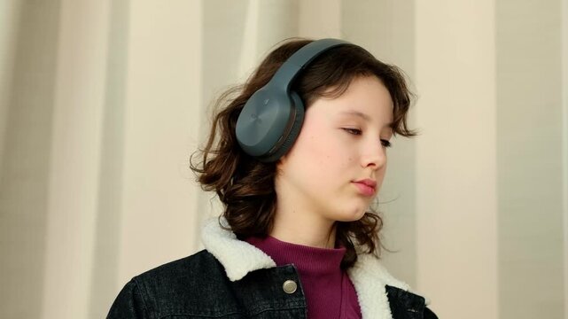 Teen girl in big wireless headphones listening to music with eyes down, relaxing and calming her thoughts after stressful school day, tema teenage music as way to cope with stress.