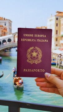 M&atilde;o segurando passaporte italiano com Veneza ao fundo. Canal com gondola tradicional, ponte hist&oacute;rica e edif&iacute;cios cl&aacute;ssicos venezianos. Ideal para viagem na europa turismo e cidadania italiana