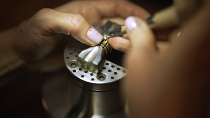 Jeweler fixing diamond into golden ring setting.