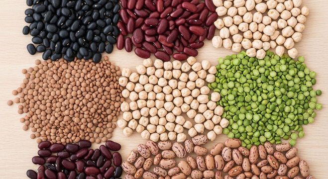 Assortment of colorful dried beans and legumes, including black beans, kidney beans, white beans, chickpeas, lentils, pinto beans, and peas, arranged in a visually appealing grid on a light wooden