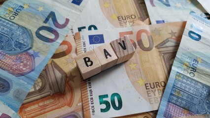 BAV acronym made of wooden letter cubes on pile of Euro banknotes. Betriebsrentenversicherung...