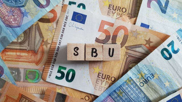 SBU acronym made of wooden letter cubes on pile of Euro banknotes. Selbstbehalt-Unfallversicherung (Self-Contribution Accident Insurance)