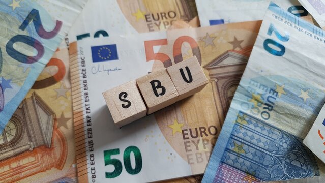 SBU acronym made of wooden letter cubes on pile of Euro banknotes. Selbstbehalt-Unfallversicherung (Self-Contribution Accident Insurance)