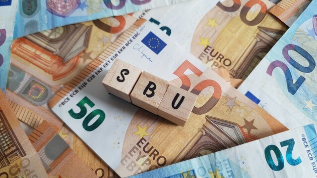 SBU acronym made of wooden letter cubes on pile of Euro banknotes. Selbstbehalt-Unfallversicherung (Self-Contribution Accident Insurance)