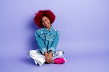 Young girl with red hair wearing denim jacket and metallic pants posing against purple background