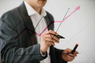 Businessman drawing rising financial chart on glass board
