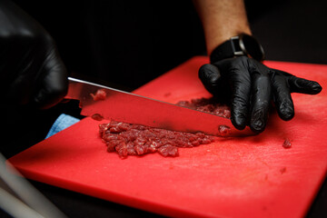 Chef slicing raw beef with knife on red cutting board