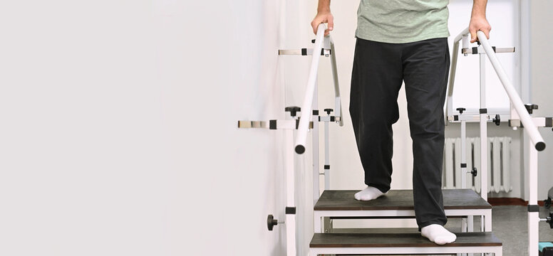A man undergoes rehabilitation after an injury on a stair climber with parallel bars at a clinic under the supervision of a physical therapist. banner
