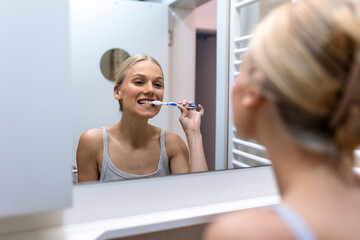 Woman Brushing Teeth in Bathroom Mirror. Dental hygiene and oral care concept, People with daily health routine. Attractive woman smiling and cleaning teeth with toothbrush in front of mirror.