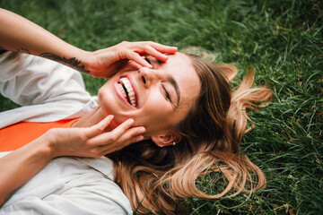 Naklejka premium Young woman lying in grass smiling outdoors enjoying a sunny day park fashion lifestyle and leisure moments