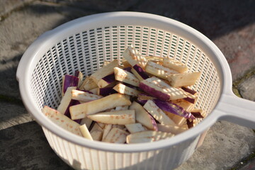 Sliced eggplant pieces draining in white plastic colander outdoors
