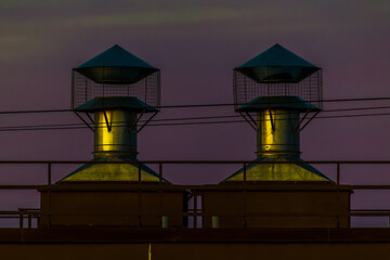 Twin rooftop ventilation chimneys glowing at dusk, creating a minimalist industrial skyline.