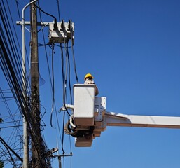 Electrical lineman team worker on hydraulic bucket truck lift performing maintenance repair on high voltage load break switch control box automation system of power distribution grid.
