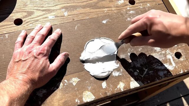 Applying filler to a wooden surface with a putty knife.