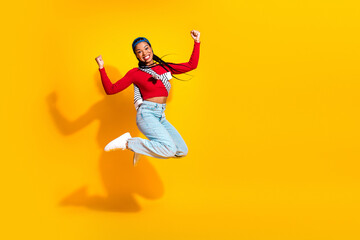 Fototapeta premium Young woman leaps in the air against a bright yellow background showcasing bold fashion and joyful energy