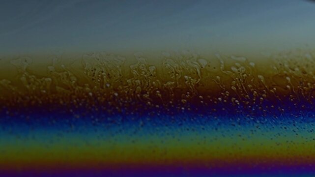 Macro video of a soap bubble surface showing dancing iridescent colors and smooth fluid motion. Abstract liquid patterns shift organically across a dark background, creating  ethereal, calming visual