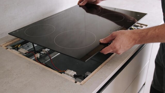 Technician installing glass ceramic induction cooktop in modern kitchen countertop, hands aligning panel for repair service, home improvement upgrade for new year renovation