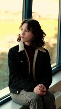 Lonely teenage girl sits alone at the window during autumn day, hugging her knees and silently thinking how to cope with problems and lack of support. Concept mental health and inner struggle of
