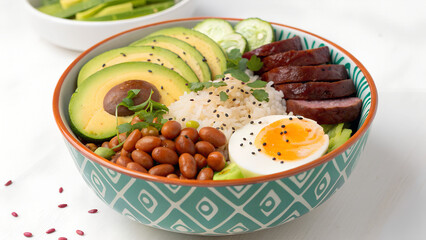 A colorful bowl presentation with avocado, beans, rice, egg and sausage.