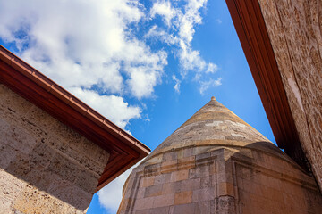 Low-angle view captures the magnificent historical Seljuk tomb in Beysehir, Turkey. Defined by its massive stone conical dome reaching toward the bright sky.