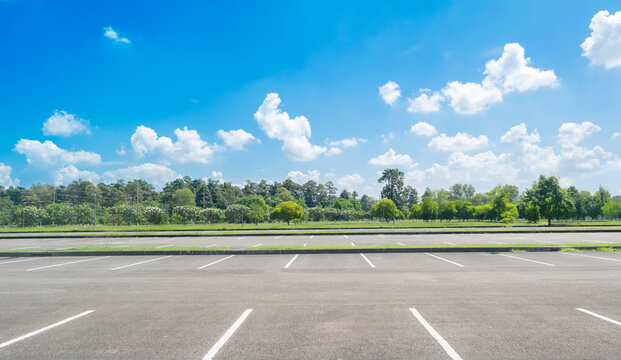 Wide empty asphalt parking lot background with white painted lines marked lens. Outdoor empty space parking lot with trees and cloudy sky. outside parking lot in a park