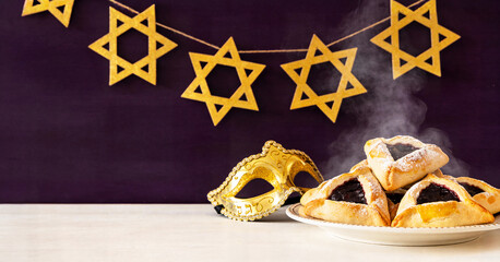 The concept of celebrating Purim (Jewish carnival holiday). Traditional hamantaschen cookies with powdered sugar, a golden garland of hexagrams, a golden mask with space for text