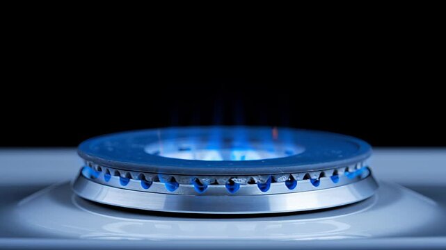 Blue flames of gas burner ignite and dance above the metallic surface, showcasing the intensity and heat of the flame in a dark kitchen setting