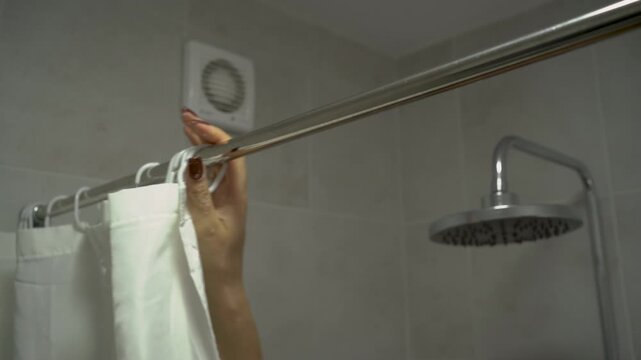 Close-up of woman hand opens the shower curtain in the bathroom.