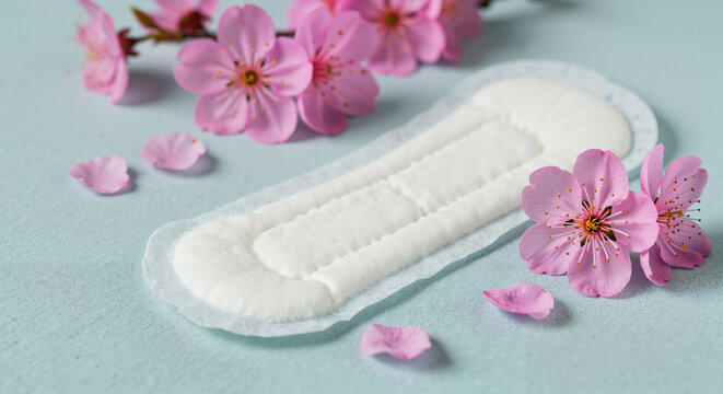 Sanitary pad surrounded by pink flowers on a light blue surface  
