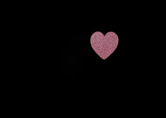 Obraz premium Single pink glitter heart placed on black background with large copy space. Minimal composition representing romance, tenderness and emotional connection.