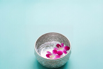 Traditional silver bowl with water and purple orchid flower for Songkran festival celebration and Thai New Year ritual on turquoise background with copy space for spa promotion