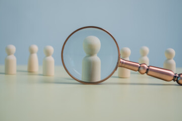 Obraz premium Wooden human figures with a magnifying glass symbolize recruitment, talent search, human resources, candidate selection, hiring process, leadership, and business decision concept.