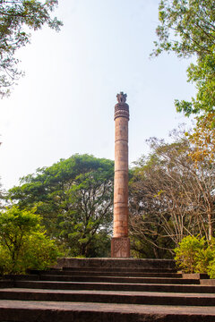 Ancient Ashokan pillar at Dhauli, Odisha rises on stepped platform, crowned with lion capital, surrounded by greenery, symbolizing Mauryan heritage, peace, and Buddhism.
