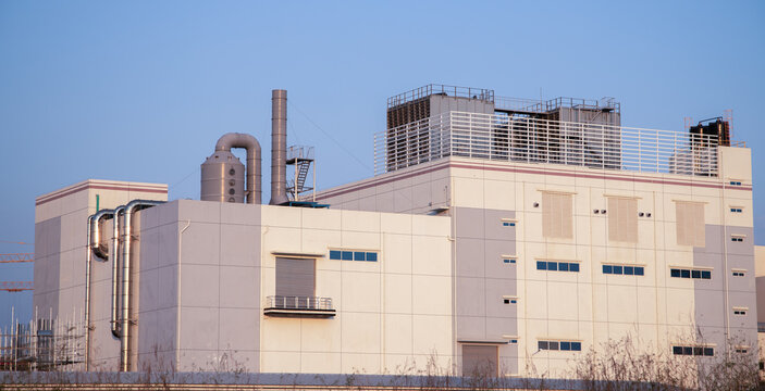 Exterior view of a large pharmaceutical or high-tech manufacturing plant in an industrial zone.Construction site of a contemporary industrial warehouse with advanced HVAC systems on the roof.