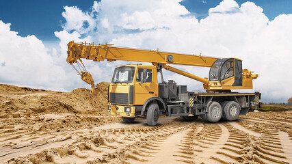 Obraz premium A truck crane is ready for work at a construction site. A large pile of sand is visible in the background, indicating ongoing construction work