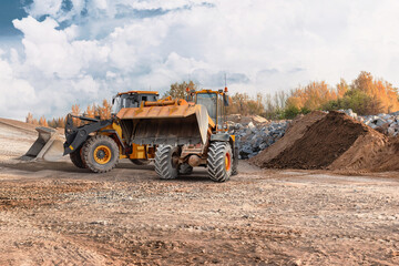 Obraz premium Loader lifts and moves dirt while excavator works on the site. Both machines are used for construction tasks. The scene is active with earth moving