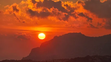 Selbstklebende Fototapeten Ziegel Dramatic sunset over the mountains of Madeira, Portugal, with glowing orange clouds and the sun setting behind a rugged island ridge, creating a warm and atmospheric landscape scene.  © Sebastiaan89