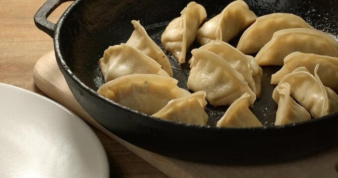 Frying pan with prepared Japanese gyoza dumplings, placed on a wooden board with a plate.