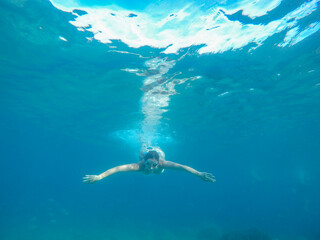 Young woman posing while swimming underwater with snorkel mask on a summer day