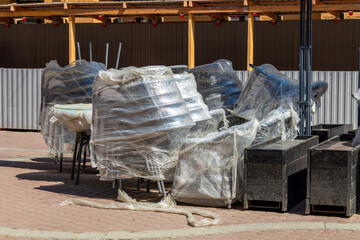 Stacked chairs and tables covered with protective film suggest a patio being shut down or stored between seasons. The scene conveys preparation, maintenance, and the quiet pause of hospitality operati