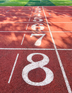 Vertical perspective of red rubber running track lane number 8 with receding start lines. Authentic outdoor stadium, ideal for sports competition, racing background, and athletic training concepts.