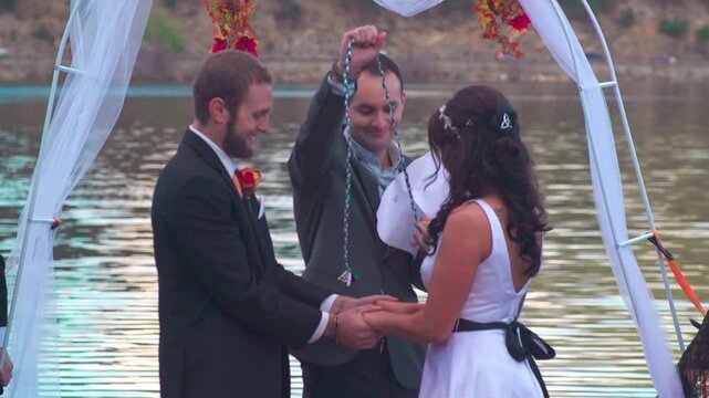 A Caucasian wedding officiant ties the groom and bride to read the blessing script during the wedding