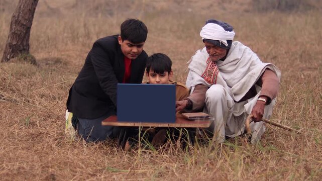 Grandfather and grandchildren sitting outdoor in nature and using laptop together.
