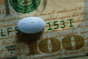 Closeup of a GLP-1 pill on a US hundred dollar bill