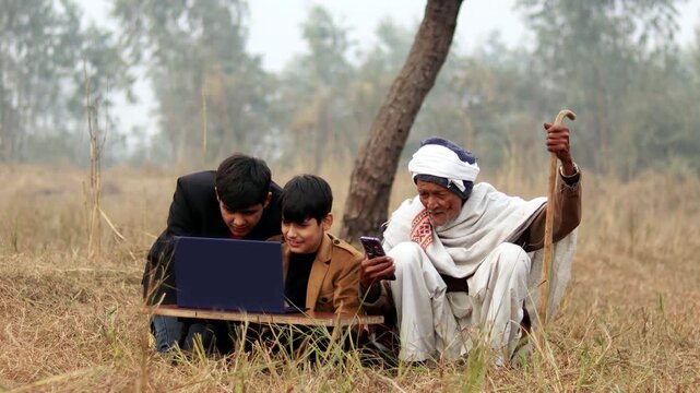 Grandfather and grandchildren sitting outdoor in nature and using laptop together and mobile phone.