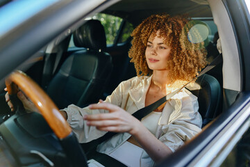 Fototapeta premium Woman with curly hair driving a car wearing a seatbelt, enjoying a sunny day and natural light, relaxed and focused on the road ahead.