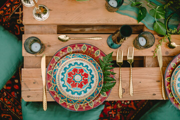 Boho table with plates, gold cutlery and candles on rustic wooden pallets