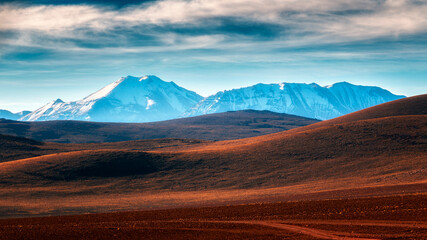 Rolling desert hills leading toward snow-capped Andean mountains under a dramatic sky in the...