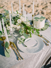 Elegant wedding table with white flowers, candles and cake on sandy beach, romantic luxury celebration setting.