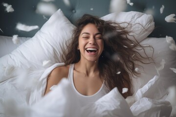 Naklejka premium Young woman laughing while feathers float around her in a playful pillow fight in bed